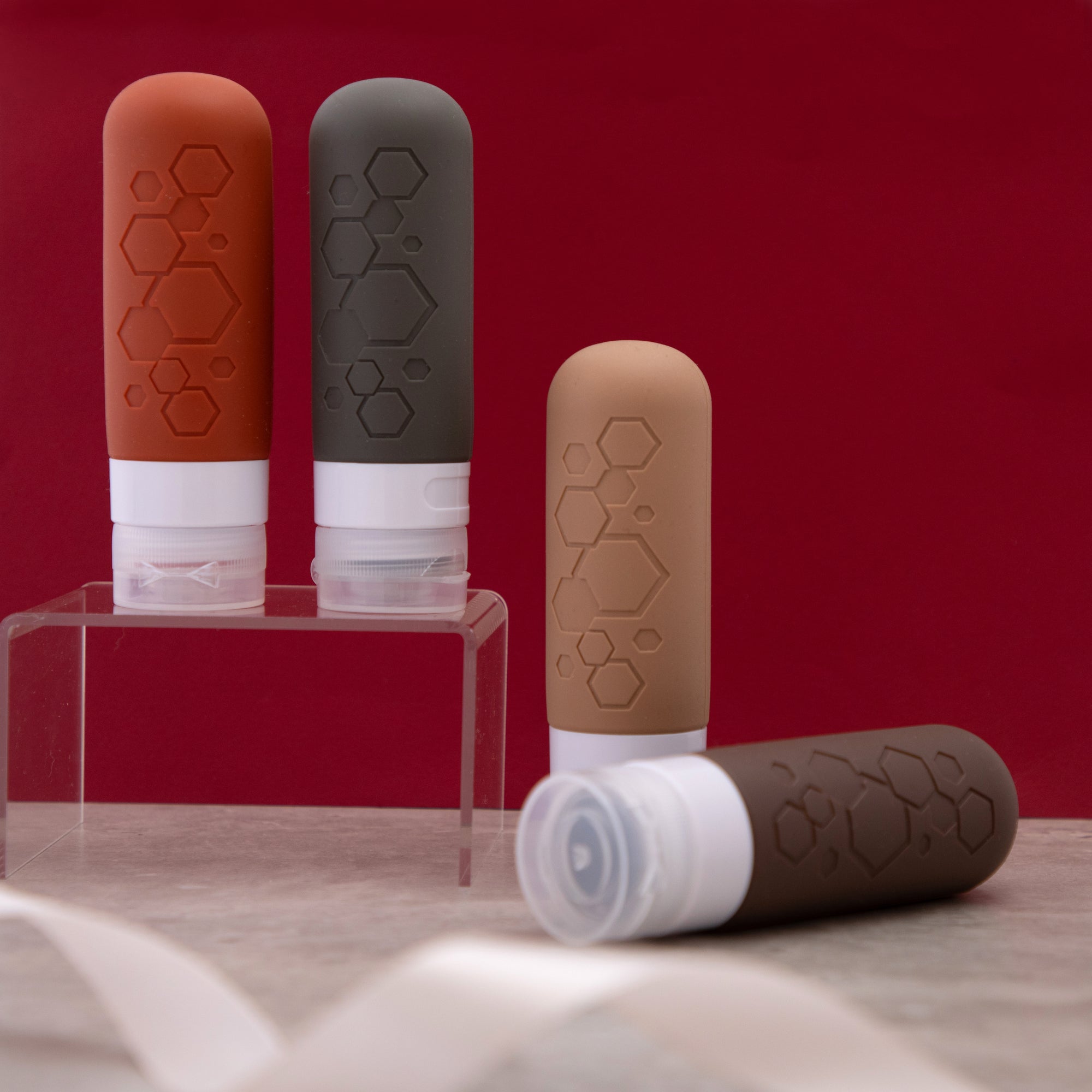 Four cylindrical containers for liquids during traveling with white bases and hexagonal patterns on a red background
