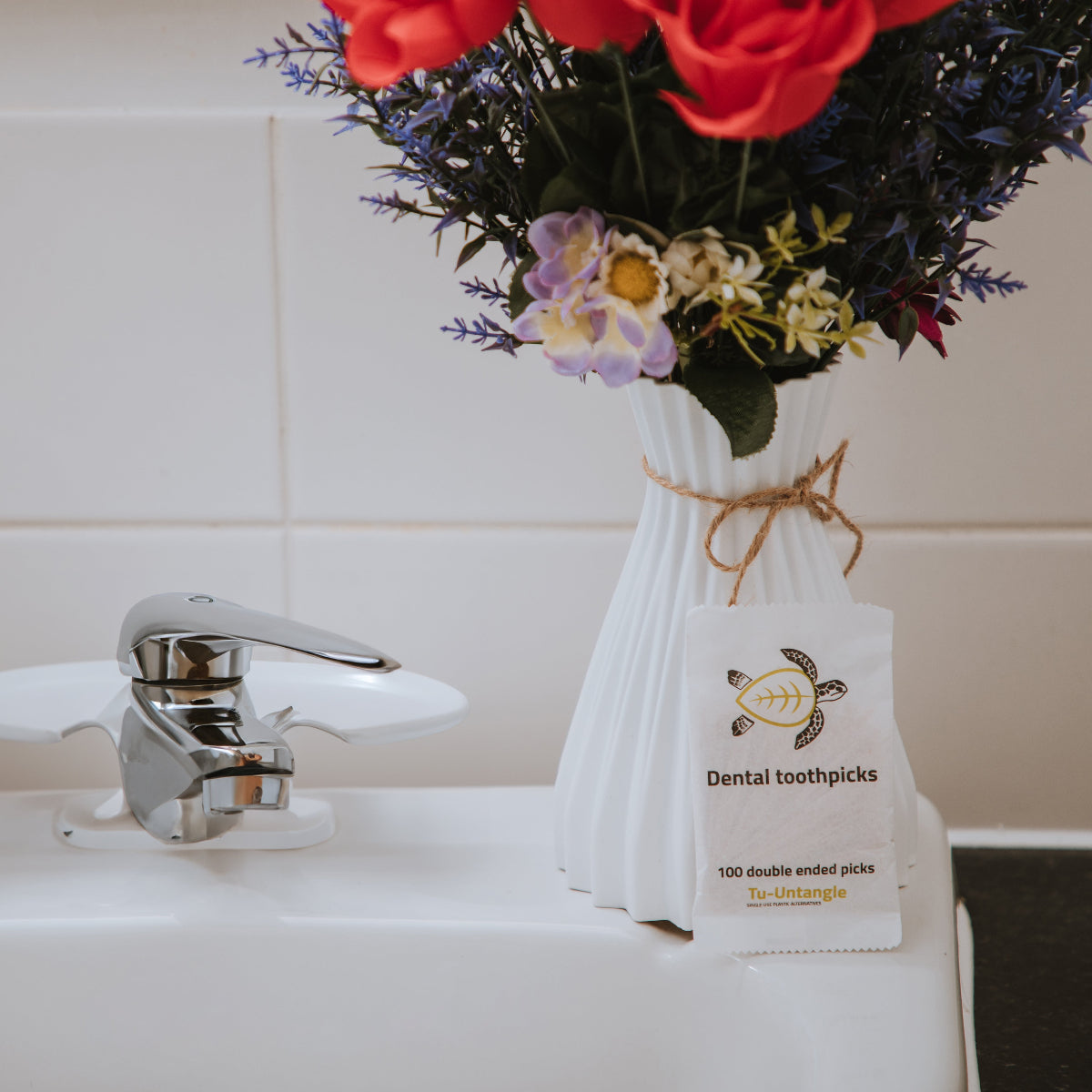 Bag of dental toothpicks with a vase of flowers on a sink